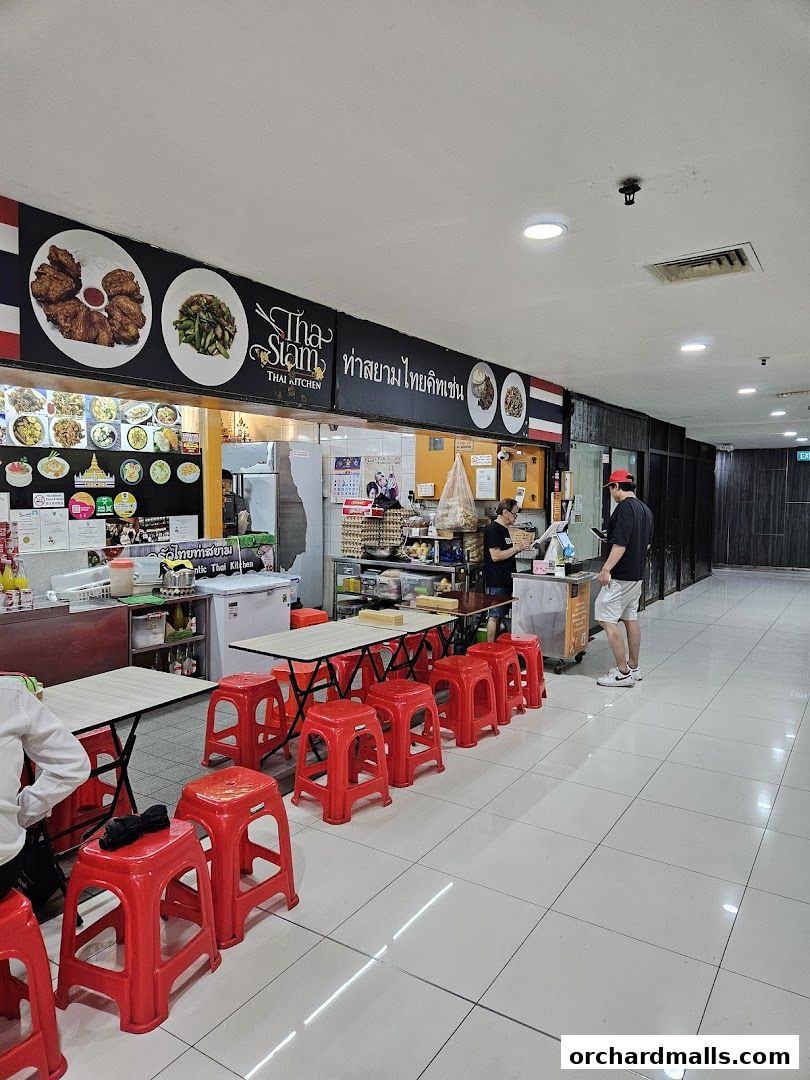 Tha Siam Thai Kitchen stall with red stools and tables, displaying food images.