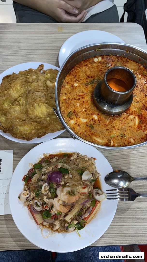 A table setting with Thai food, including Tom Yum soup, a glass noodle salad, and an omelet.