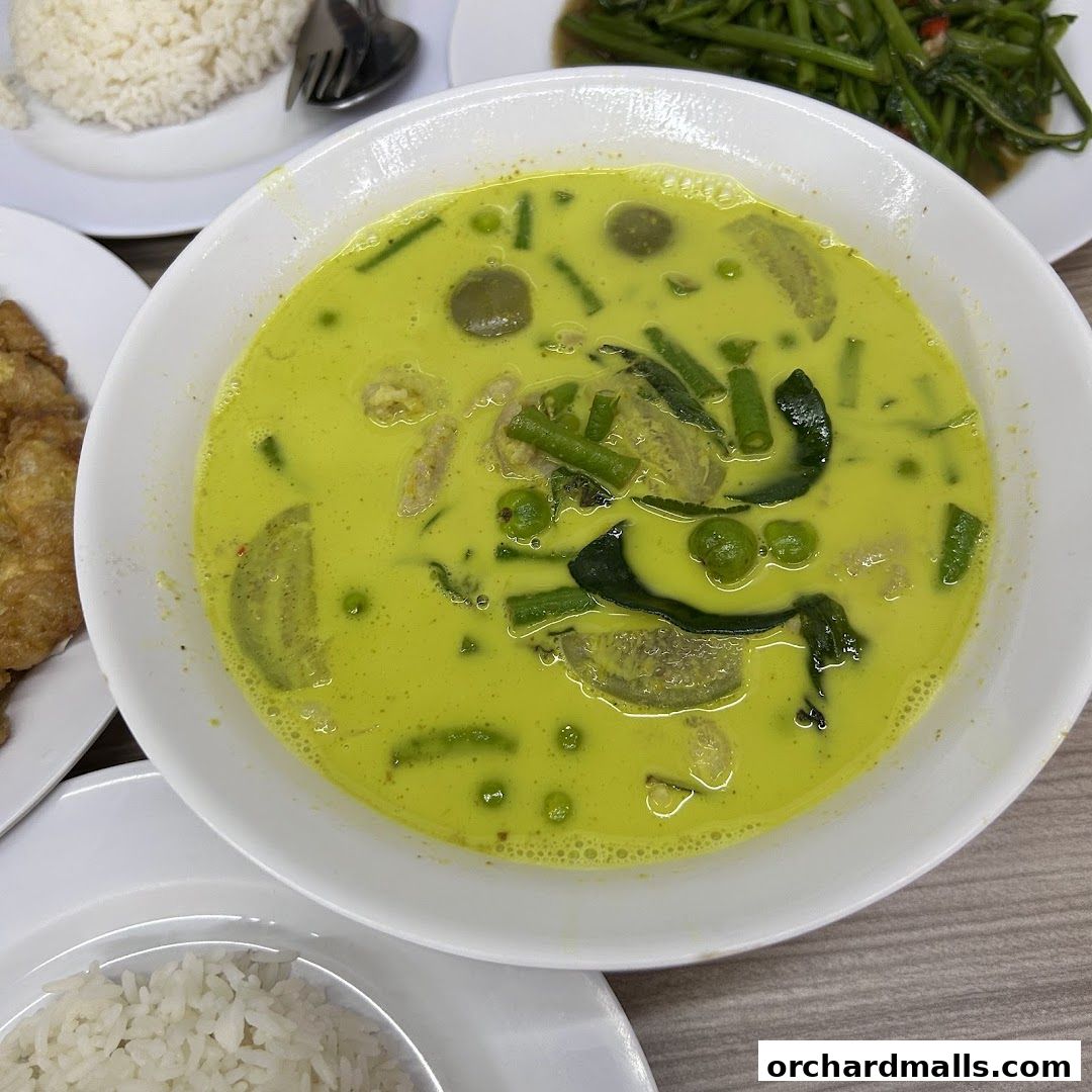 A bowl of vibrant green curry with chicken, vegetables, and rice.