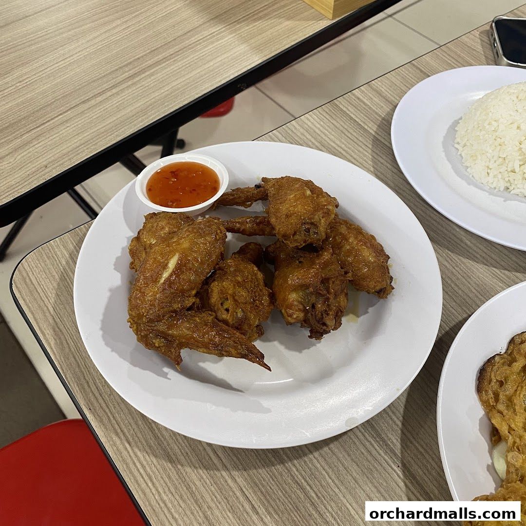 A plate of crispy fried chicken wings served with sweet chili sauce and a side of rice.