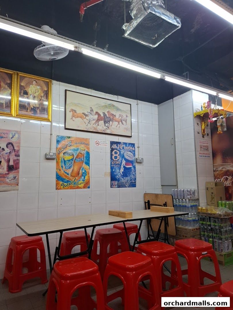 Interior of a Thai restaurant with tables, red stools, and decorative posters on the wall.