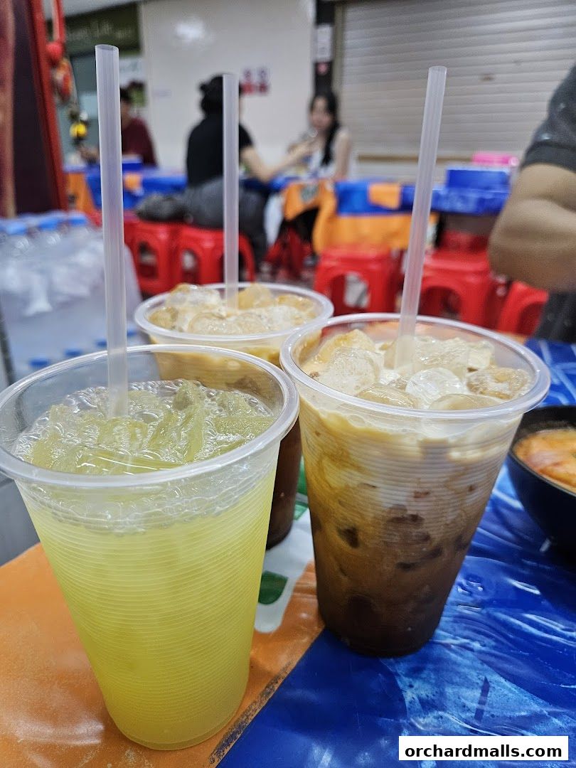 Three refreshing drinks, including iced coffee and a yellow beverage, sit on a table at Tha Siam Thai Kitchen.