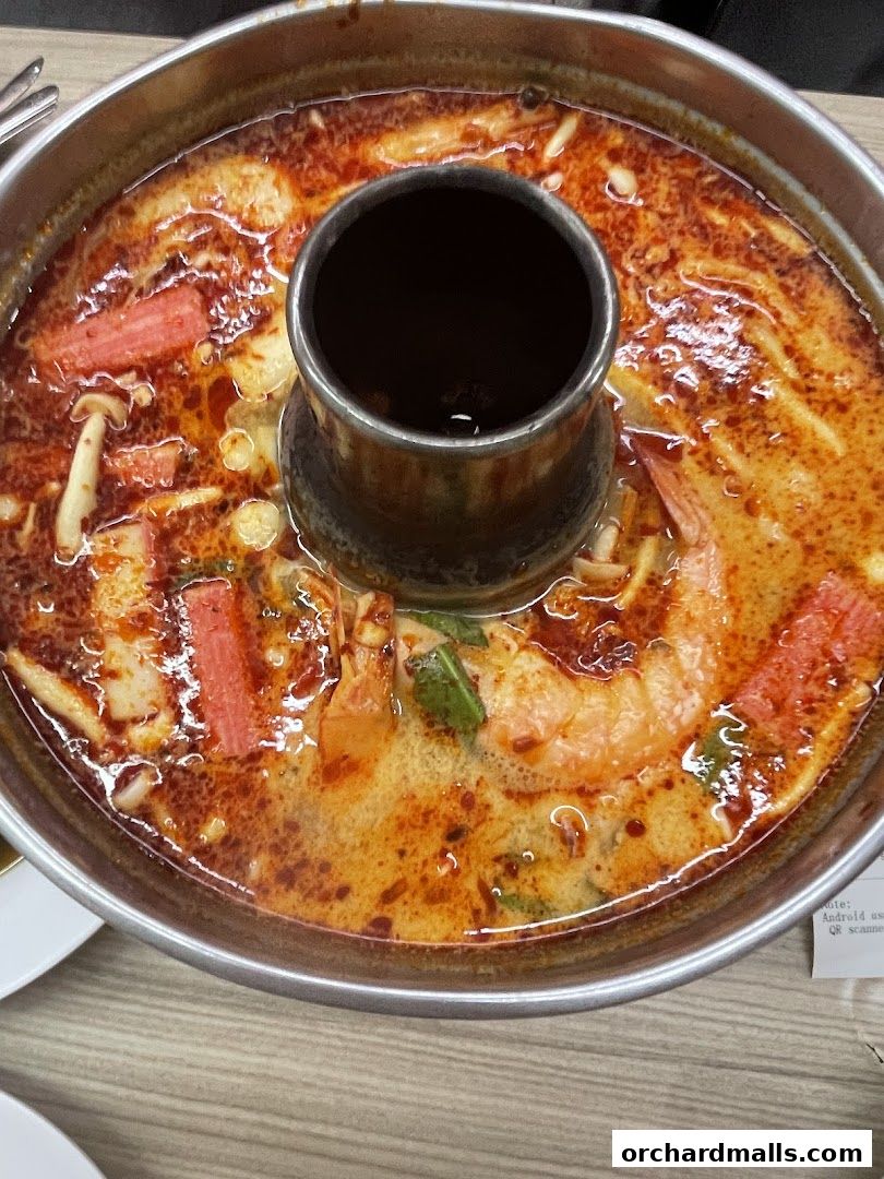 A close-up shot of a steaming pot of Tom Yum soup with shrimp and crab sticks.
