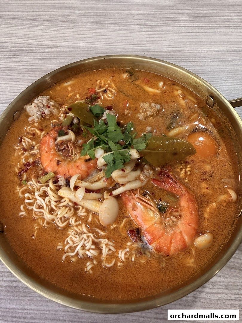 A close-up shot of a steaming bowl of Tom Yum noodles with shrimp and mushrooms.