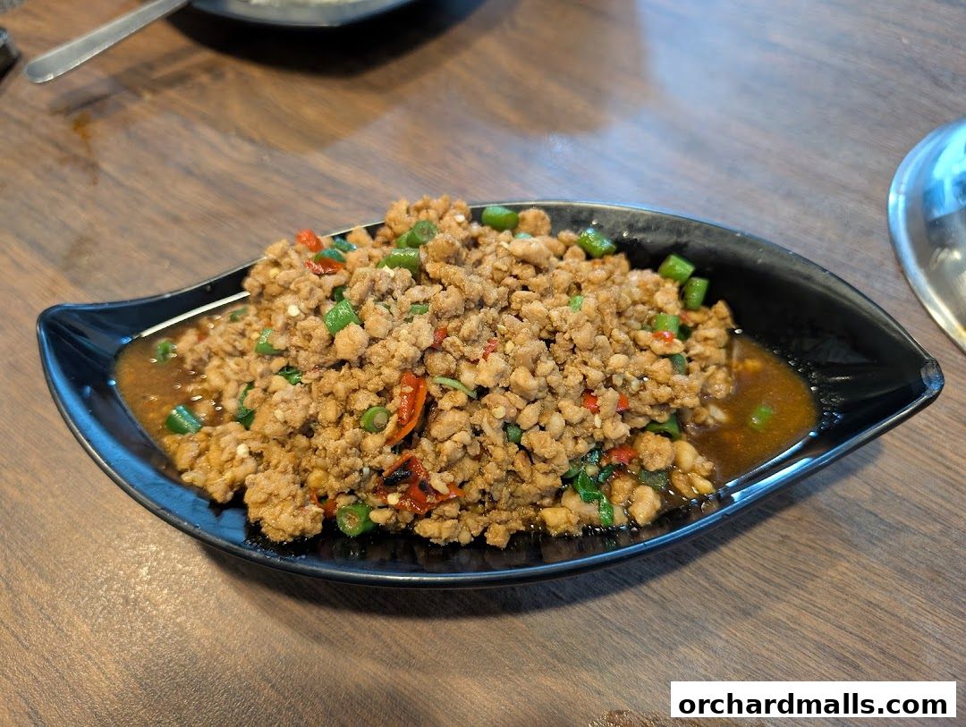 A close-up of a flavorful Thai minced meat dish served in a black bowl on a wooden table.