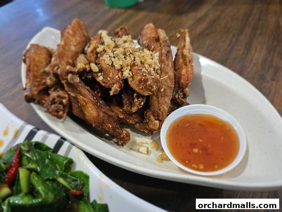 A plate of crispy fried chicken wings with a side of sweet chili sauce.