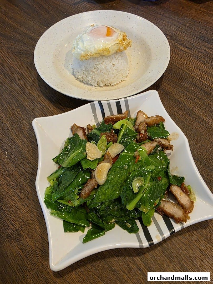 A plate of stir-fried Chinese broccoli with crispy pork and a fried egg over rice.