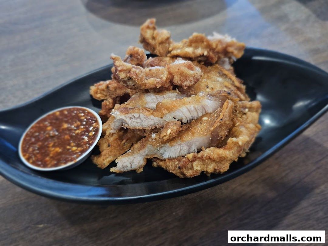 Crispy fried pork slices served with a spicy dipping sauce on a black plate.