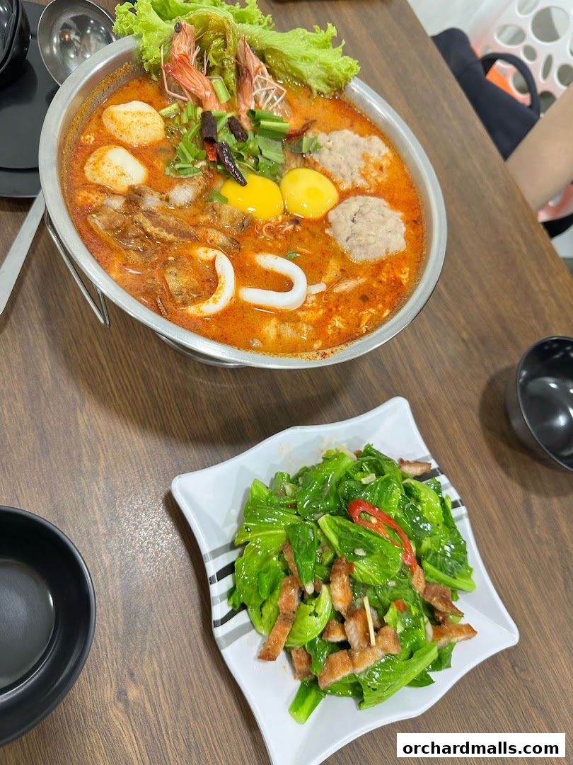 A steaming bowl of Tom Yum soup with shrimp and a side of stir-fried greens with pork.