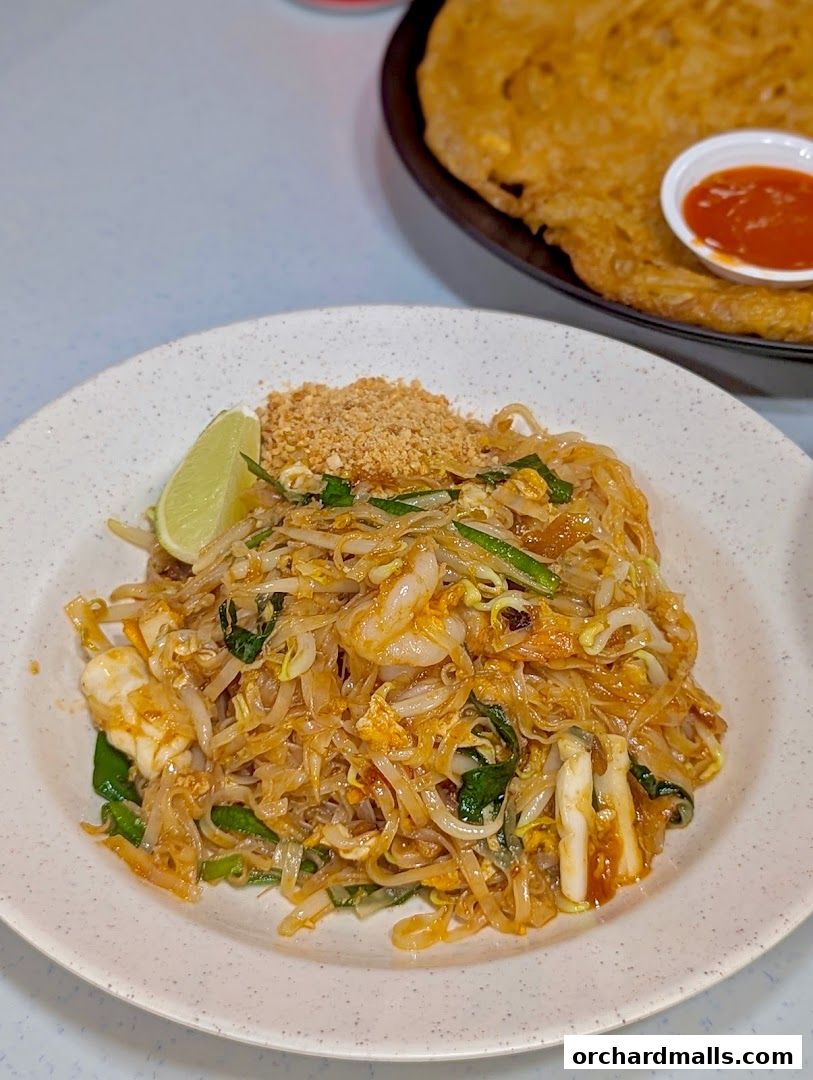 A plate of Pad Thai with shrimp and a side of chili sauce.