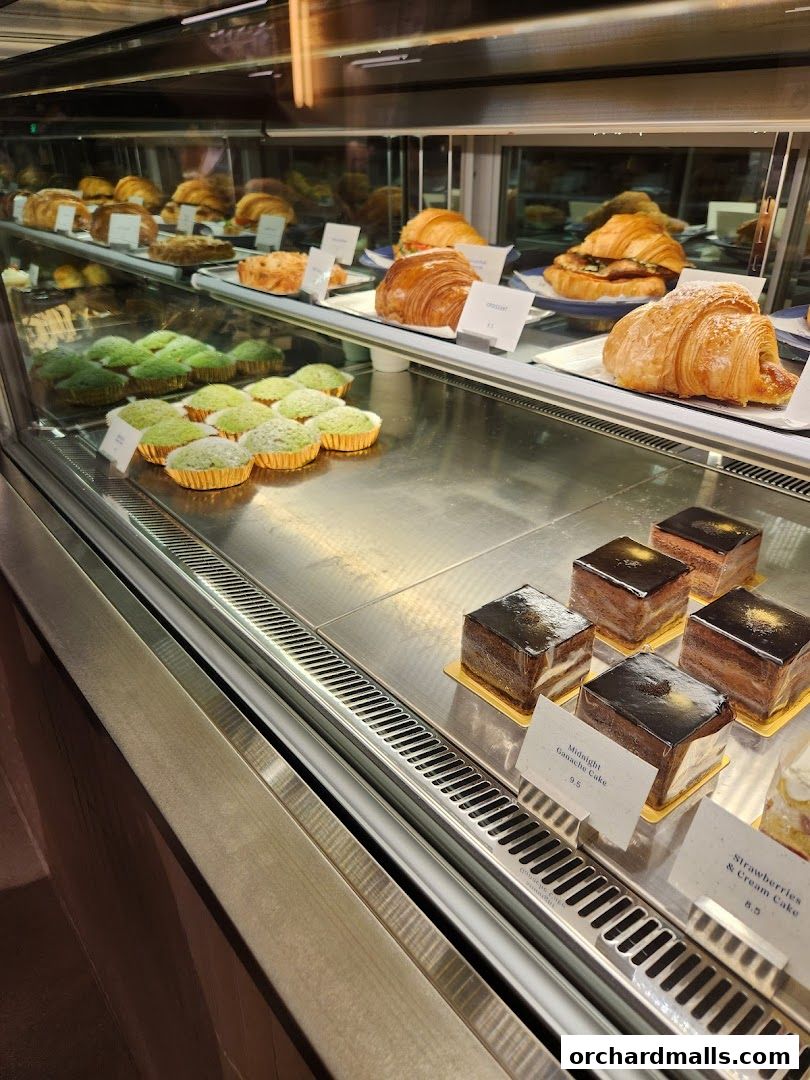 A display case filled with various pastries, including croissants, muffins, and cakes.