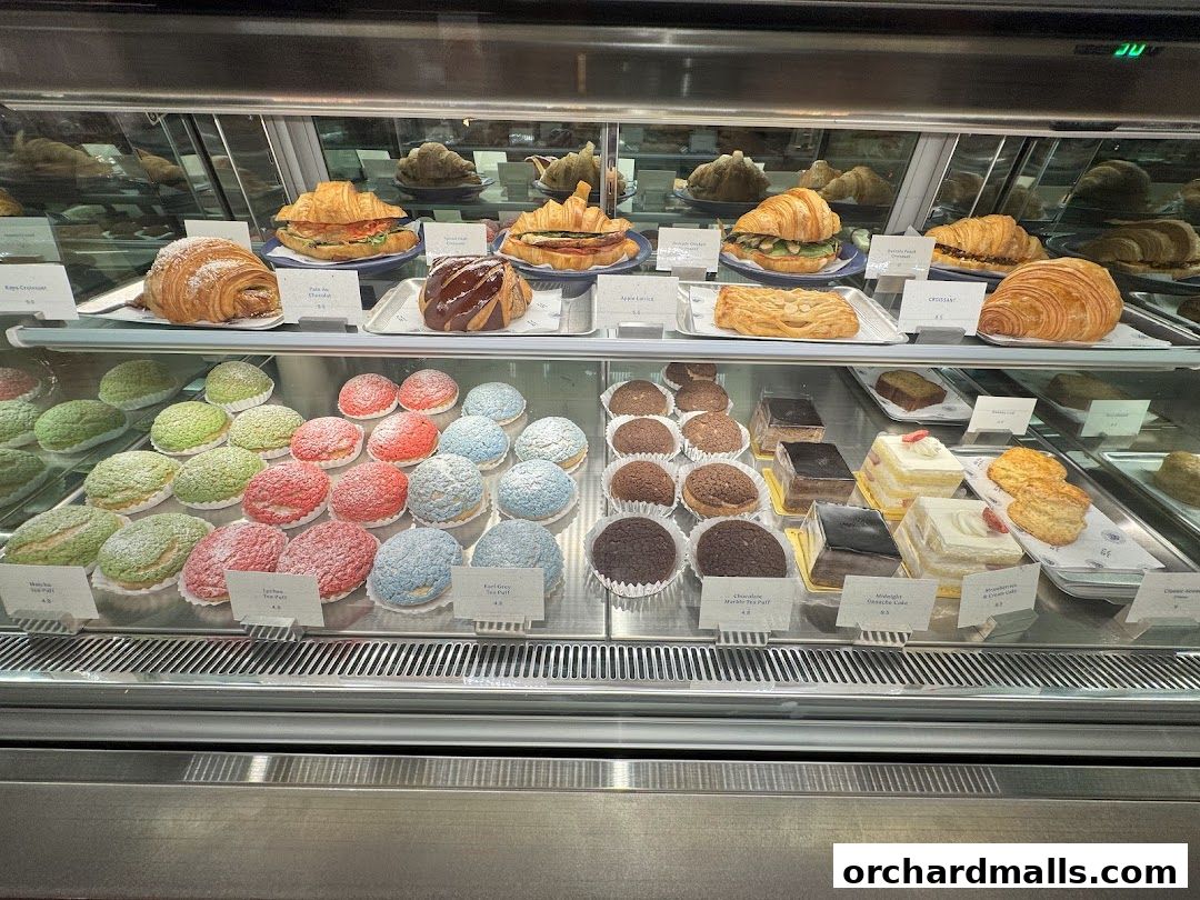 A display case filled with a variety of colorful pastries, cakes, and croissants.