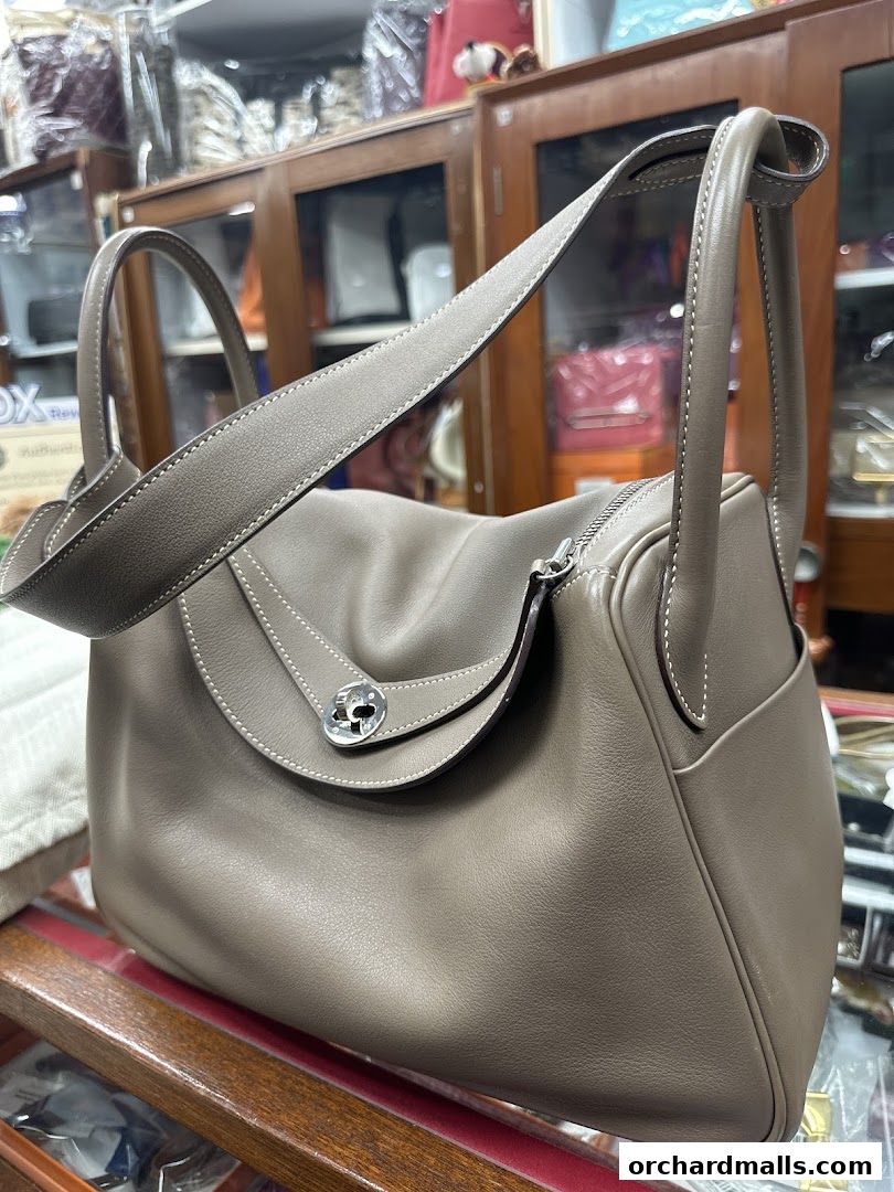 A close-up of a stylish taupe leather handbag with white stitching and silver hardware.