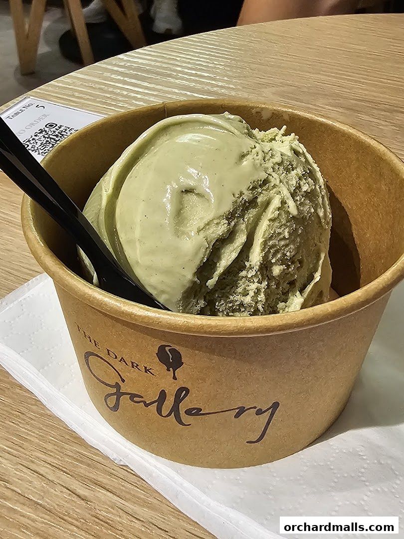 A cup of creamy green ice cream with two black spoons from The Dark Gallery.