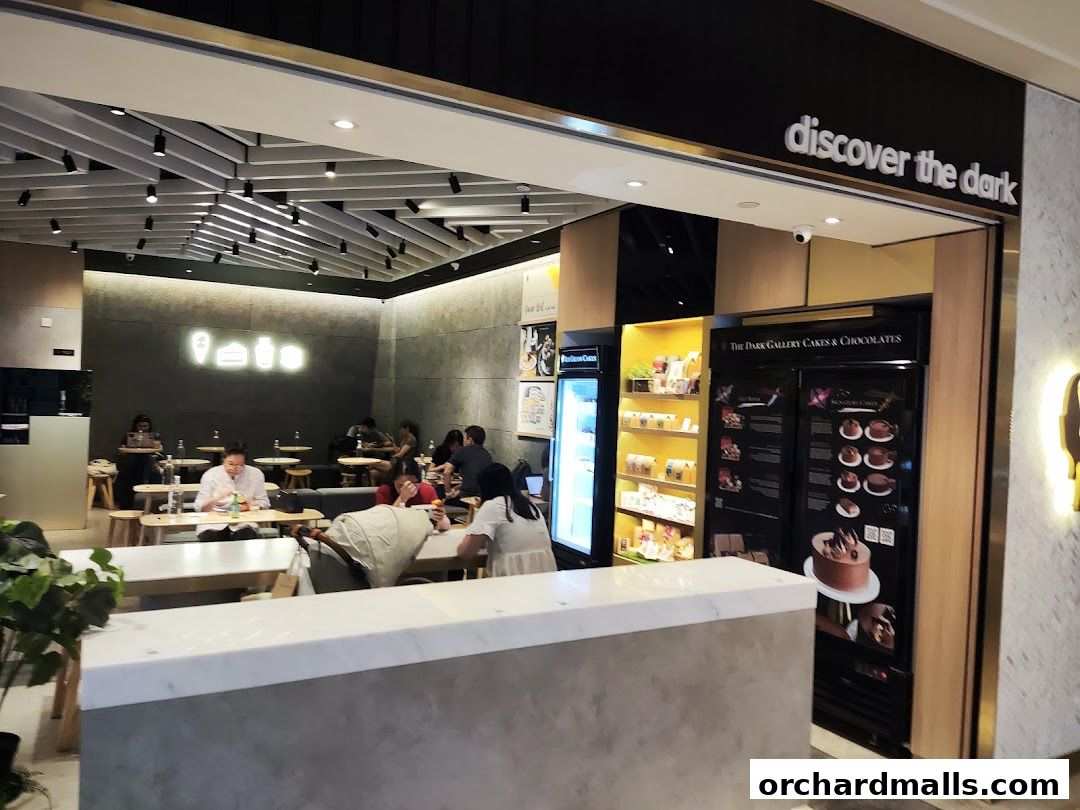 Interior of The Dark Gallery cafe with customers seated and a display of cakes and chocolates.