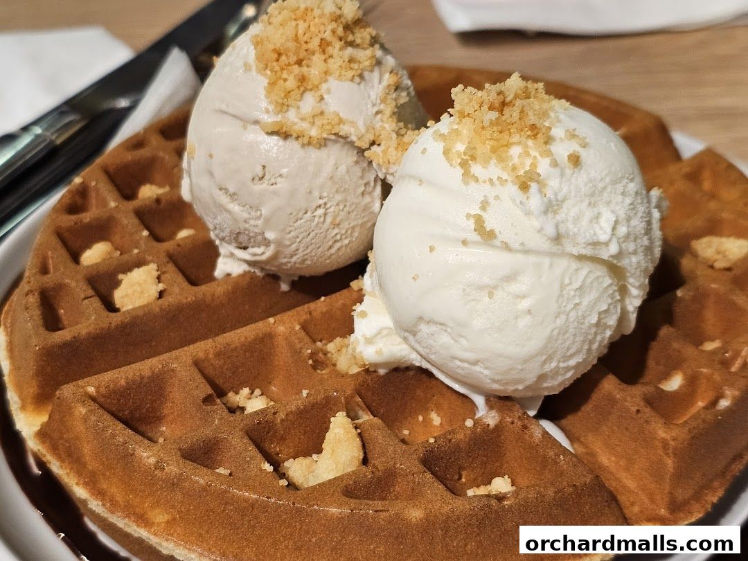 A delicious waffle topped with two scoops of ice cream and crunchy toppings.