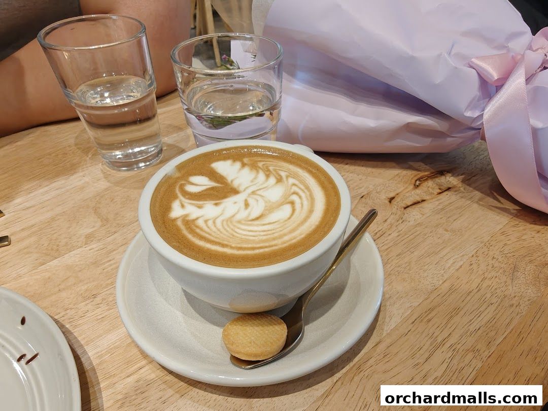 A beautifully crafted latte with art, served with a cookie and water.