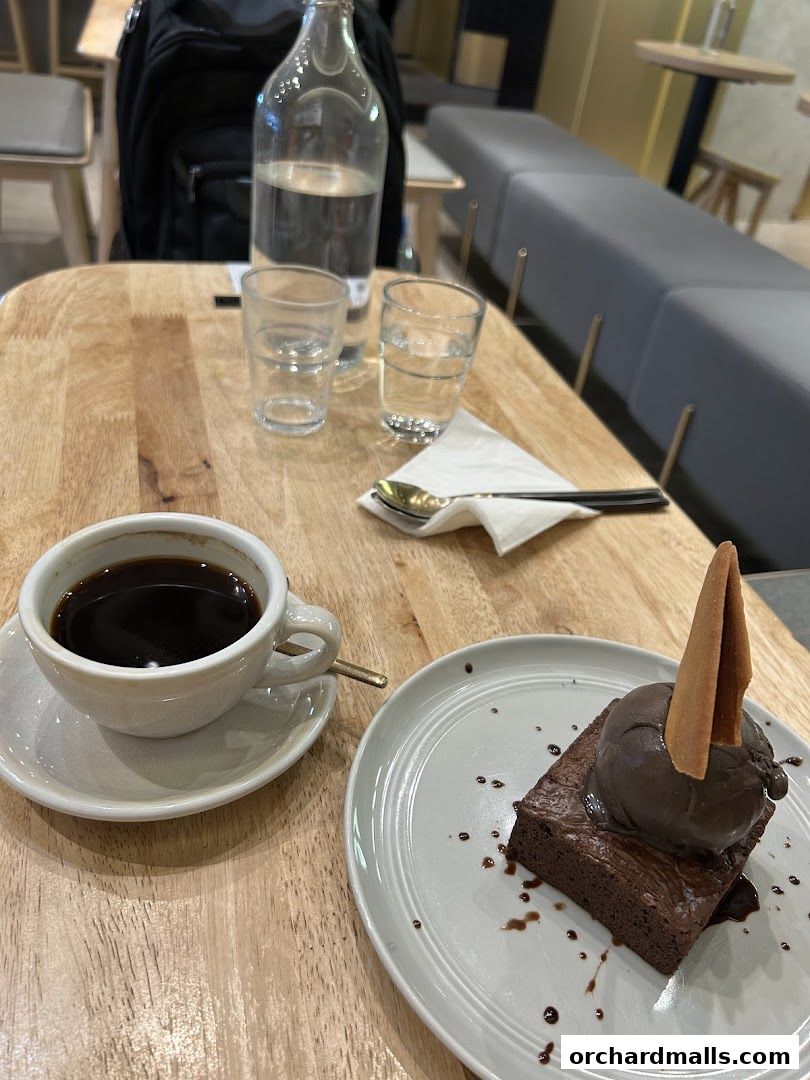 A cup of black coffee and a chocolate brownie with ice cream on a wooden table.