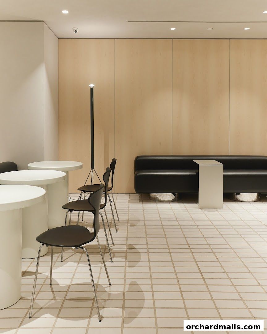 Modern interior with white tables, black chairs, and a black sofa against a wood-paneled wall.