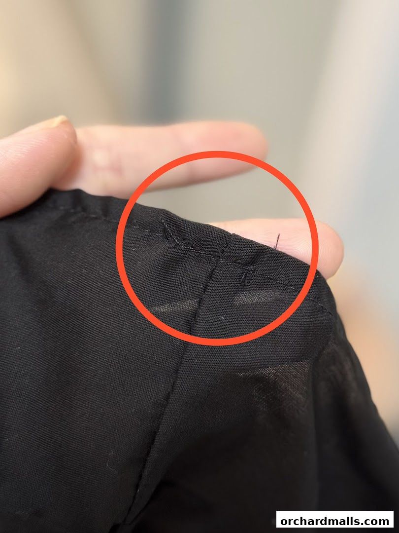 Close-up of black fabric with stitching and a loose thread, highlighted by a red circle.