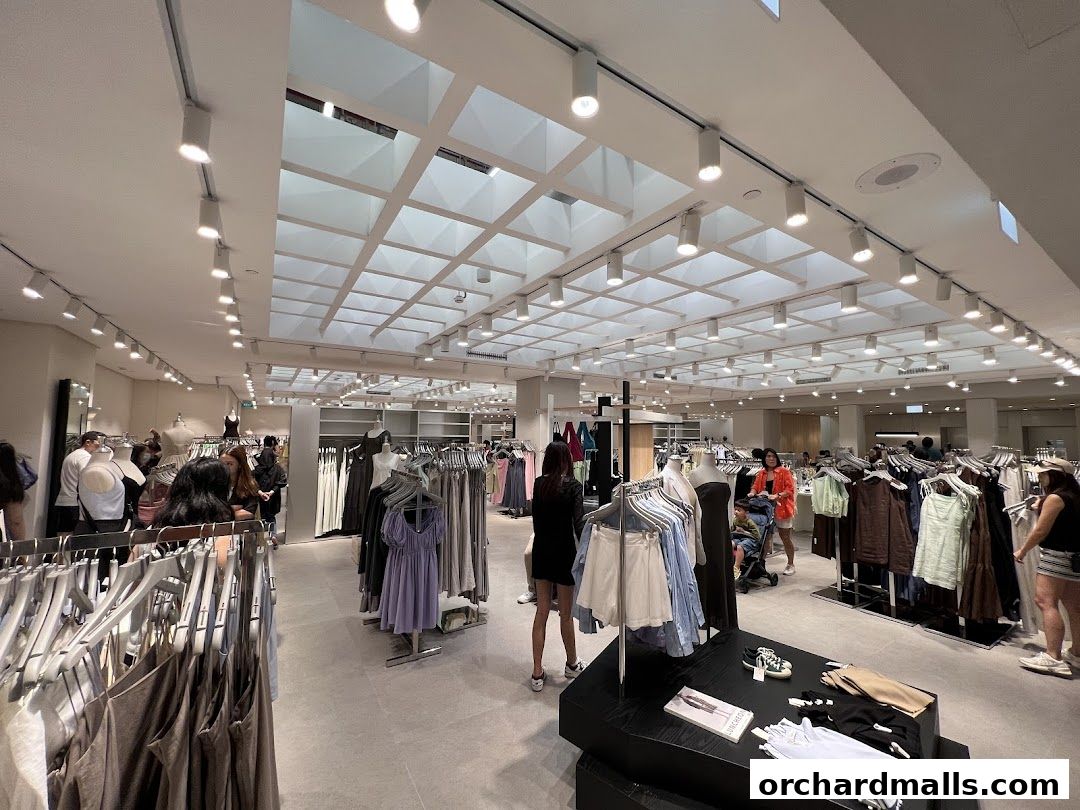 Interior view of a well-lit clothing store with racks of apparel and shoppers.