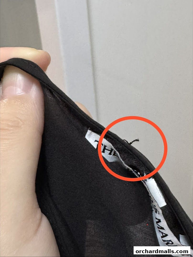 Close-up of a black garment label with a loose thread highlighted.