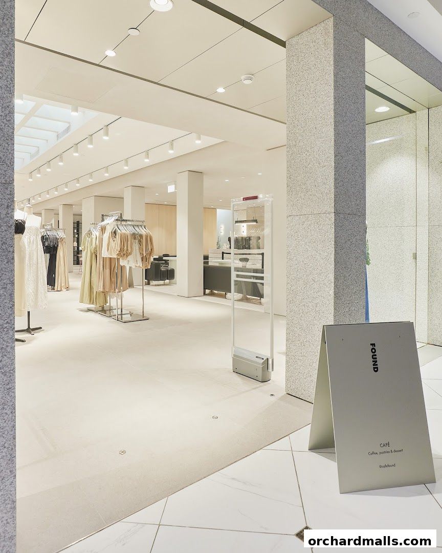 Interior of a bright, modern clothing store with racks of apparel and a cafe sign.