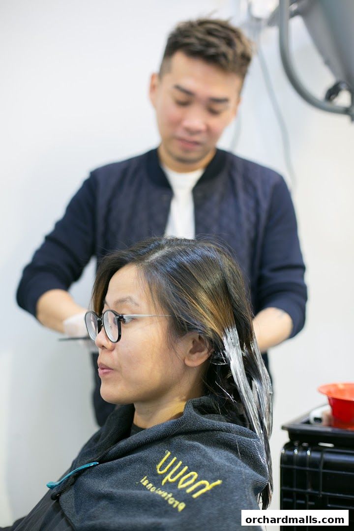 A hairstylist applies treatment to a client's hair in a salon.