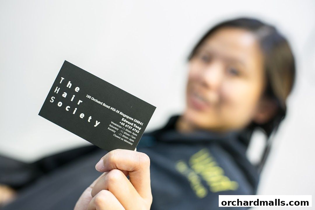 A person holds a business card for 'The Hair Society' with their contact information.