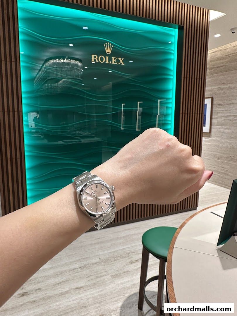 A person wearing a Rolex watch in front of a Rolex store interior.