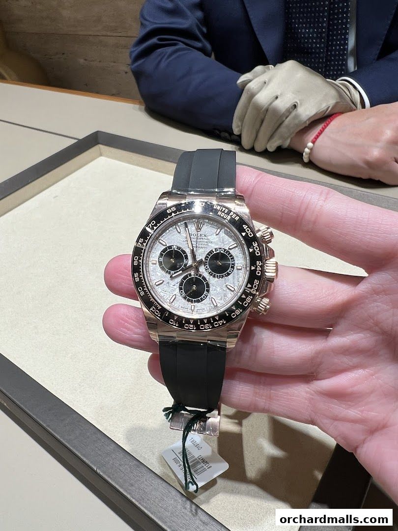 A hand holds a luxury Rolex watch with a black strap in a retail store.