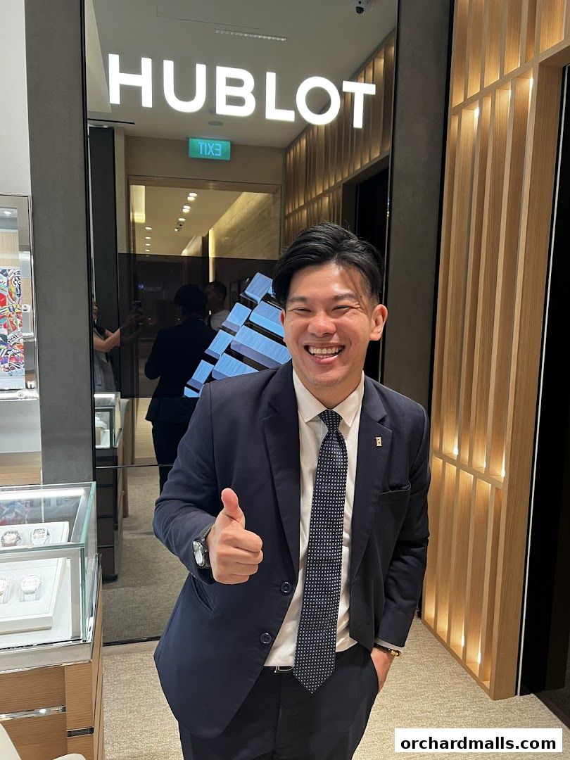 A man in a suit gives a thumbs up in front of a Hublot store.