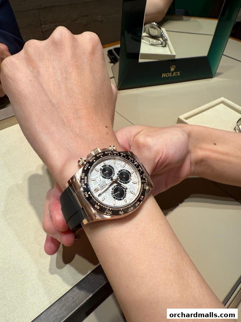 A person tries on a luxurious rose gold Rolex Daytona watch with a black strap.