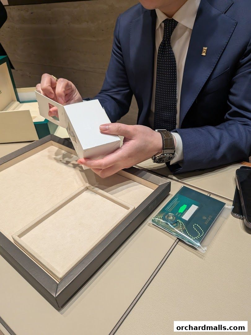 A person in a suit unboxes a luxury watch, with Rolex documentation nearby.