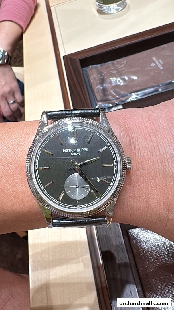 A close-up of a Patek Philippe watch on a wrist, with a display case in the background.