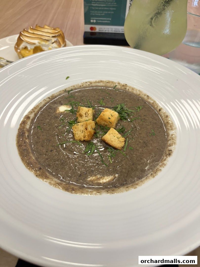 A bowl of creamy mushroom soup with croutons and herbs, next to a dessert and drink.