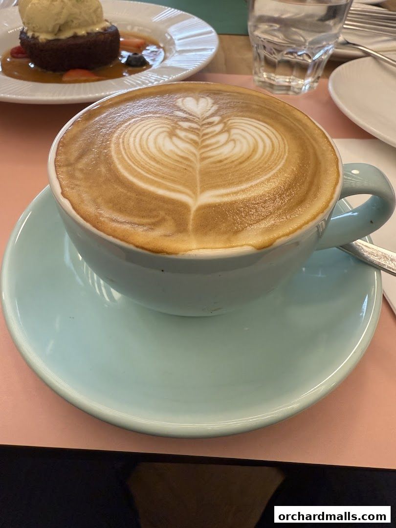 A close-up of a latte with intricate latte art, next to a dessert and a glass of water.