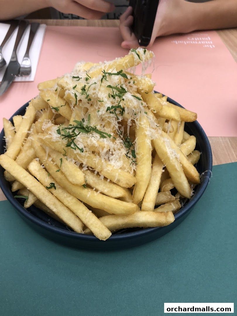 A close-up shot of a bowl of golden fries topped with grated cheese and herbs.