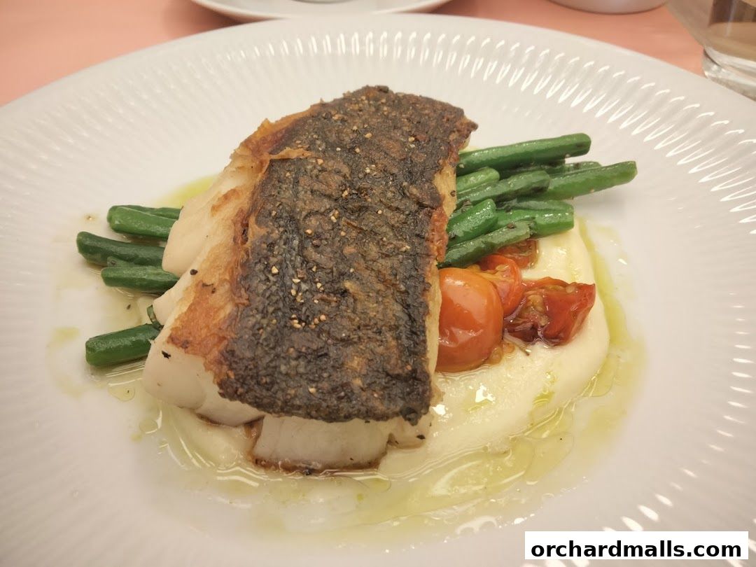 A beautifully plated dish of pan-seared fish with mashed potatoes, green beans, and cherry tomatoes.