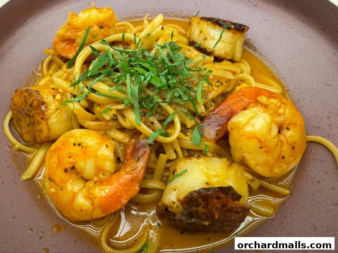 A close-up of linguine pasta with seared scallops and shrimp in a creamy sauce.