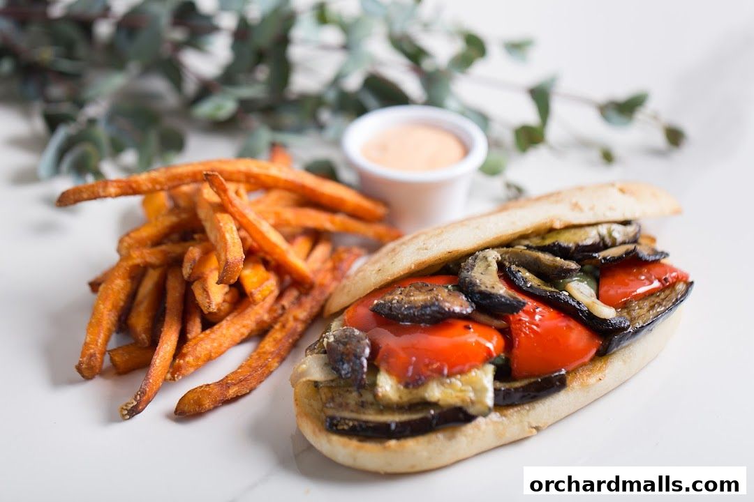 A delicious grilled vegetable sandwich with a side of sweet potato fries and dipping sauce.