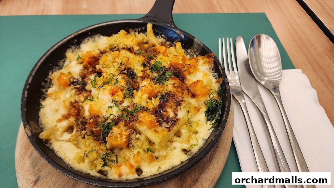 A close-up of a creamy pasta dish with pumpkin and a crispy topping, served in a cast-iron skillet.