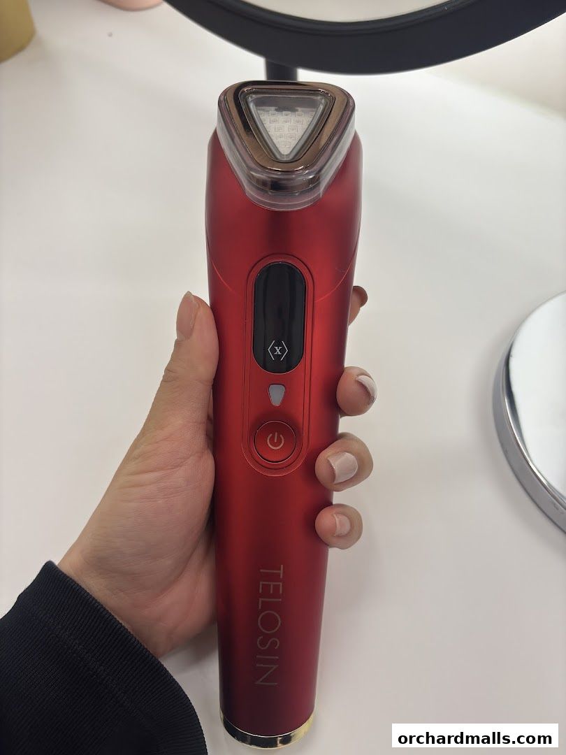 A hand holds a red beauty device with a triangular LED light panel.