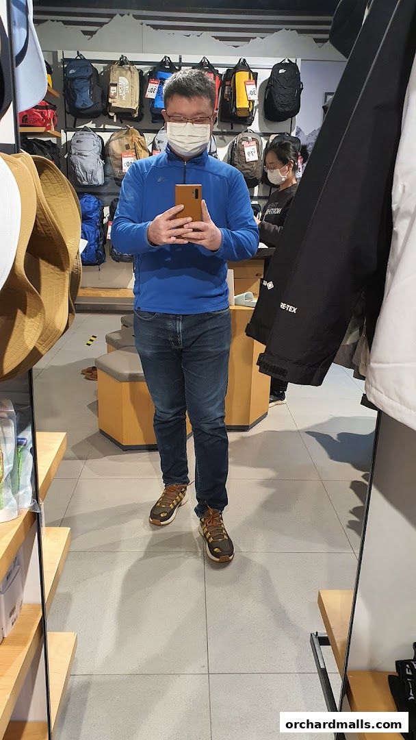 Man in a blue jacket and jeans takes a mirror selfie in an outdoor gear store.