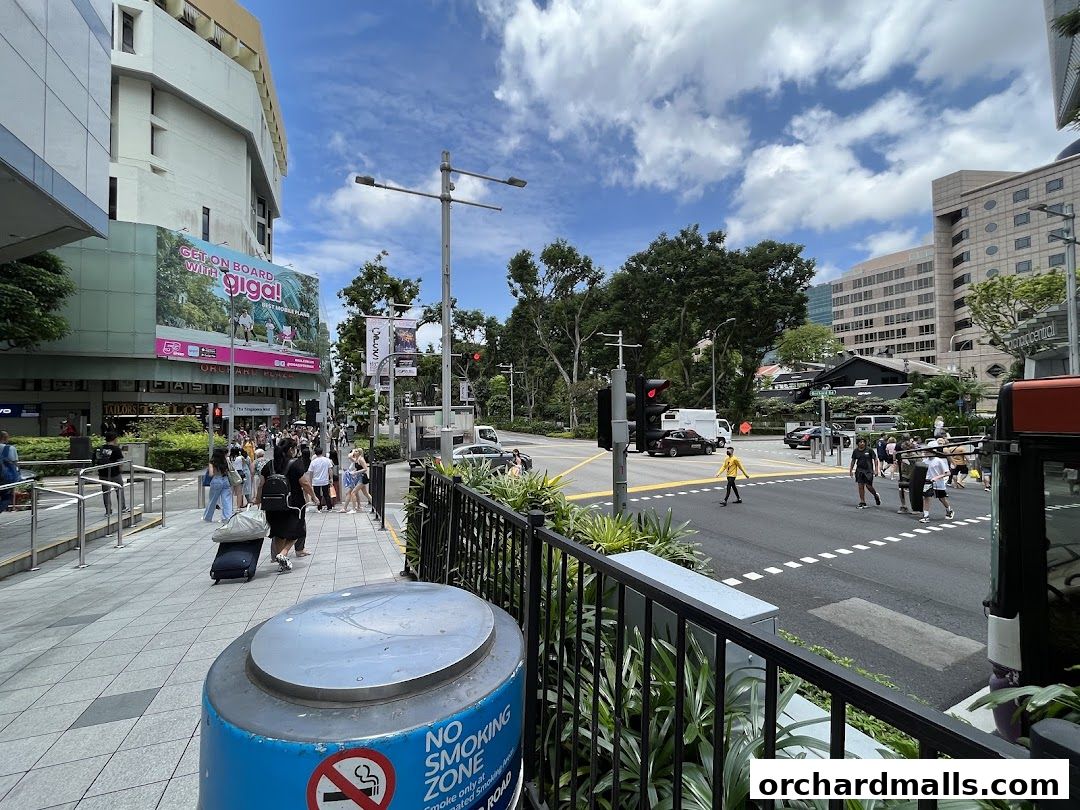 A busy street scene with pedestrians, traffic, and buildings under a cloudy sky.