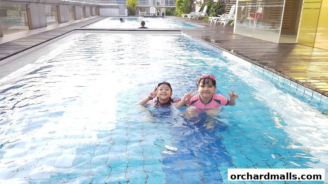 Two smiling children in swimsuits enjoy a refreshing dip in a bright blue swimming pool.
