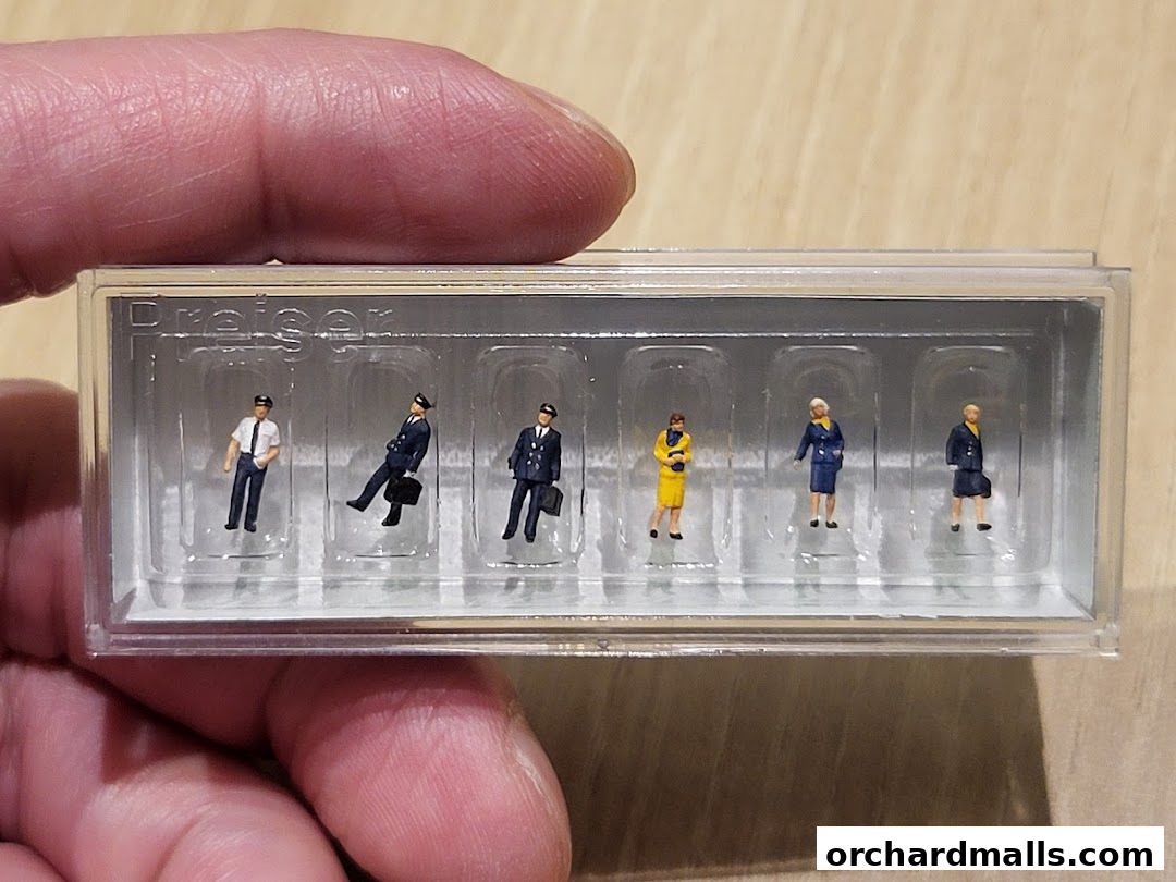 A hand holds a clear plastic case containing six miniature figures of people in uniform.