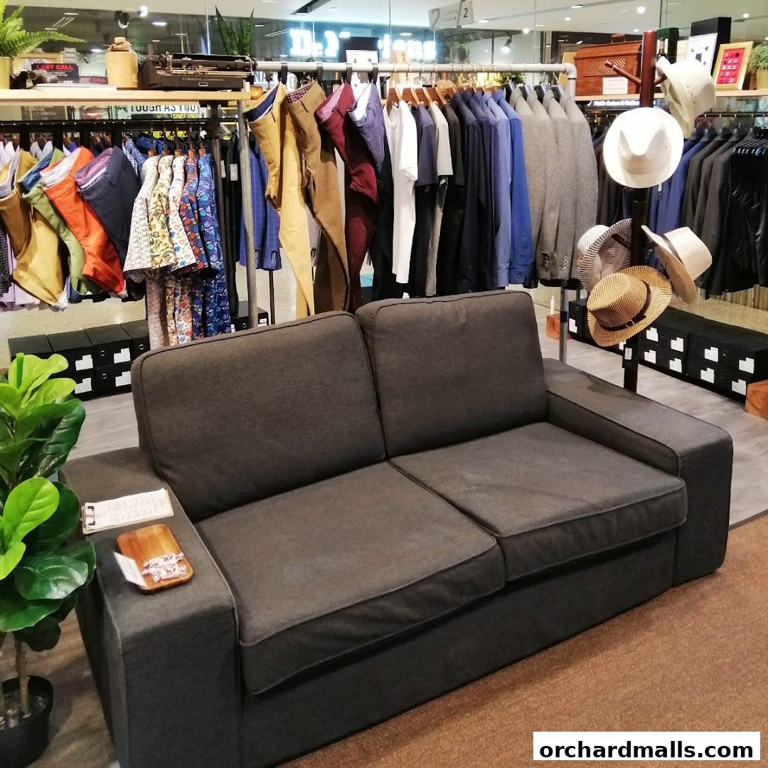 A dark grey sofa sits in front of racks of men's clothing and hats.