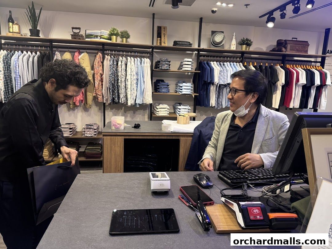 Shop staff assisting a customer at the counter with shirts displayed in the background.