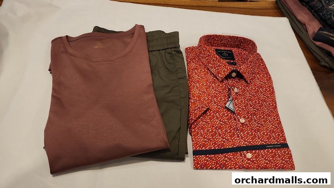 A folded rose-colored t-shirt, olive green pants, and a red patterned shirt.